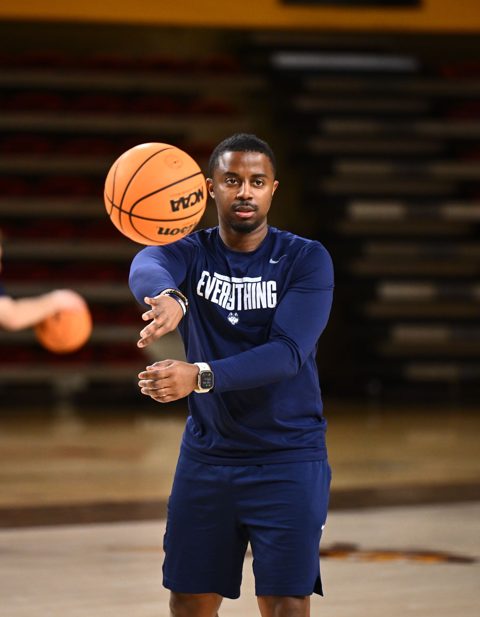 Mat Johnson '13, in a navy blue sweatsuit, throws a basketball toward someone near the camera during a practice.