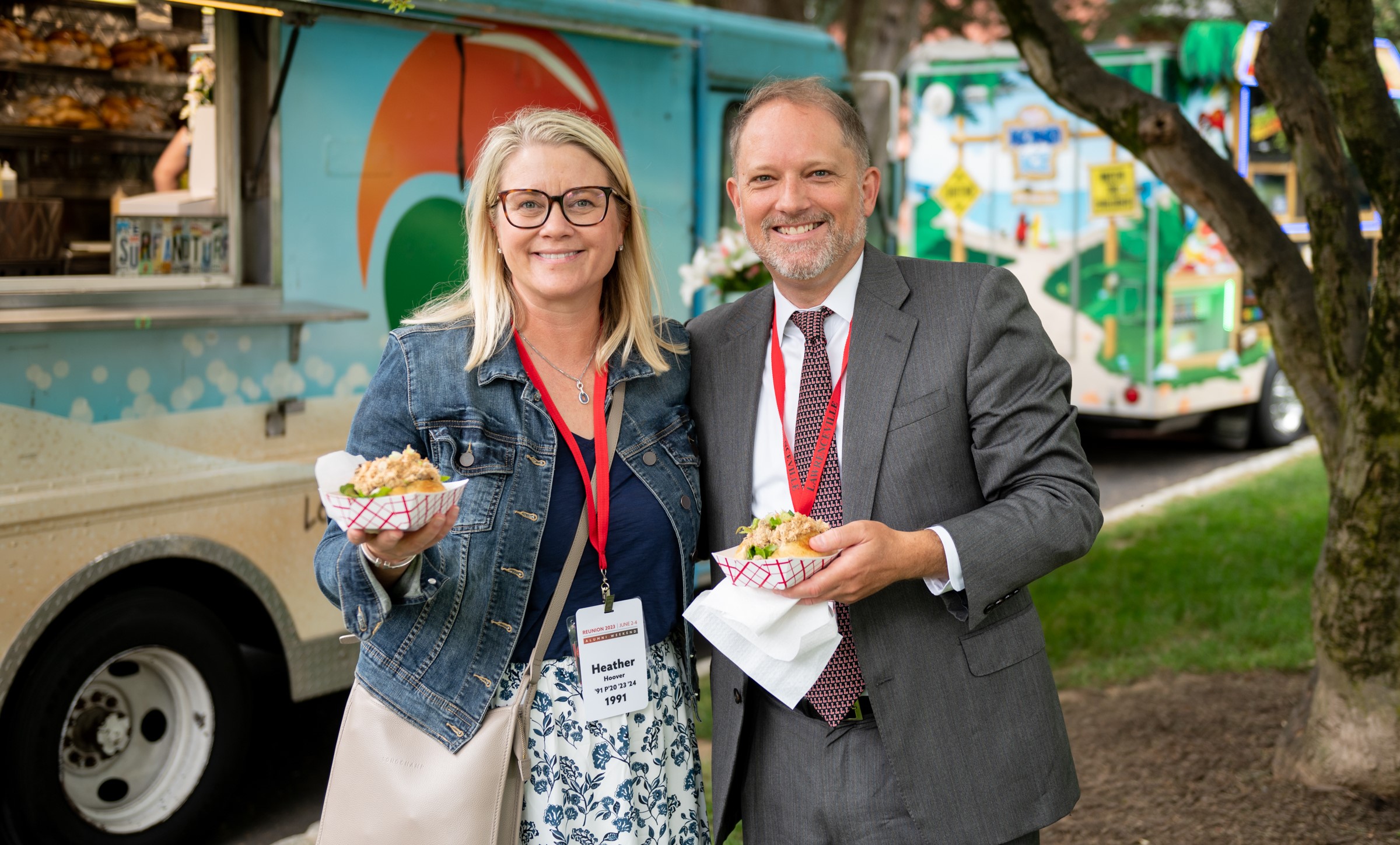 Alumni Association president Heather Hoover and her immediate past predecessor, Charlie Keller, enjoy food from a food truck while smiling at the camera during Alumni Weekend 2023.