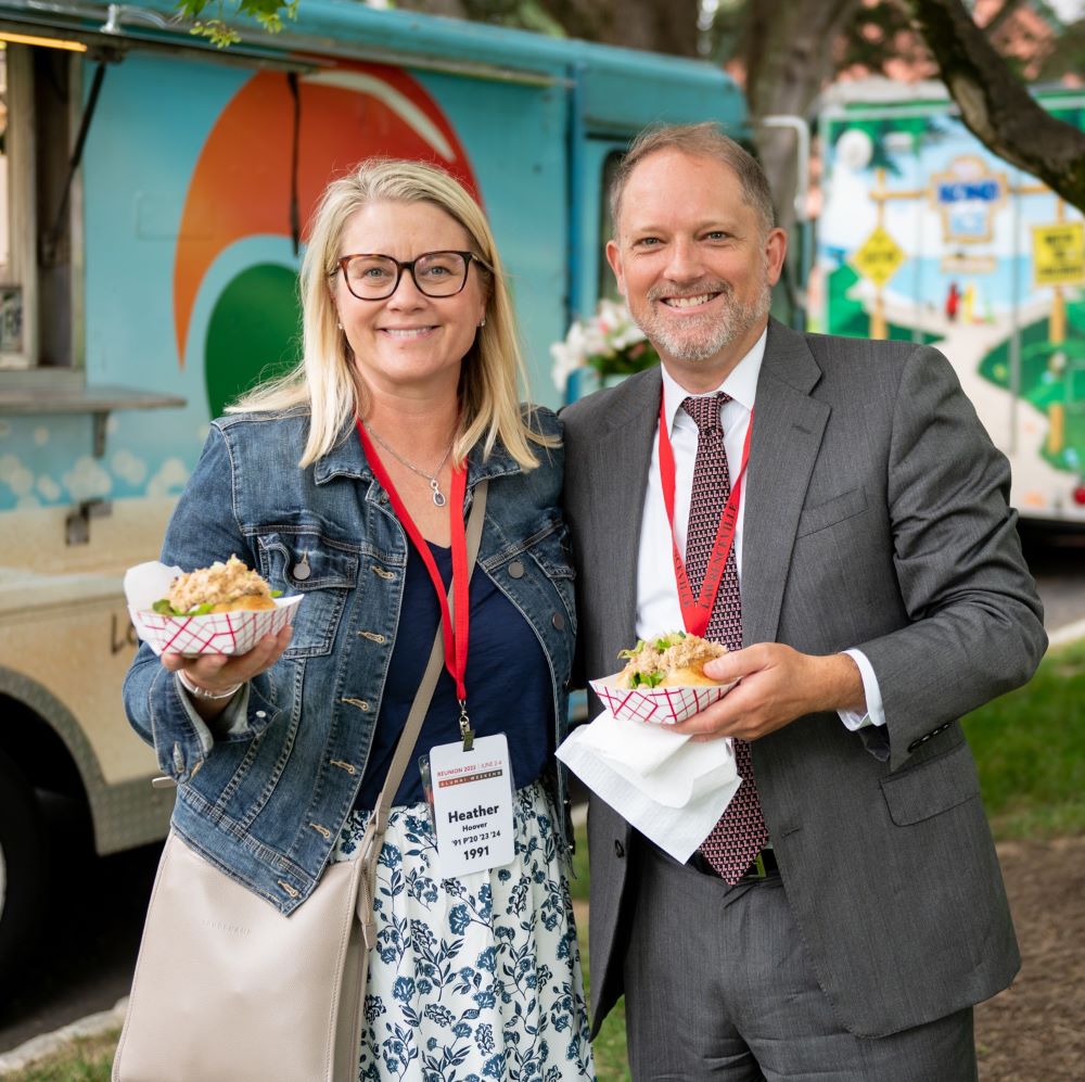 Alumni Association president Heather Hoover and her immediate past predecessor, Charlie Keller, enjoy food from a food truck while smiling at the camera during Alumni Weekend 2023.