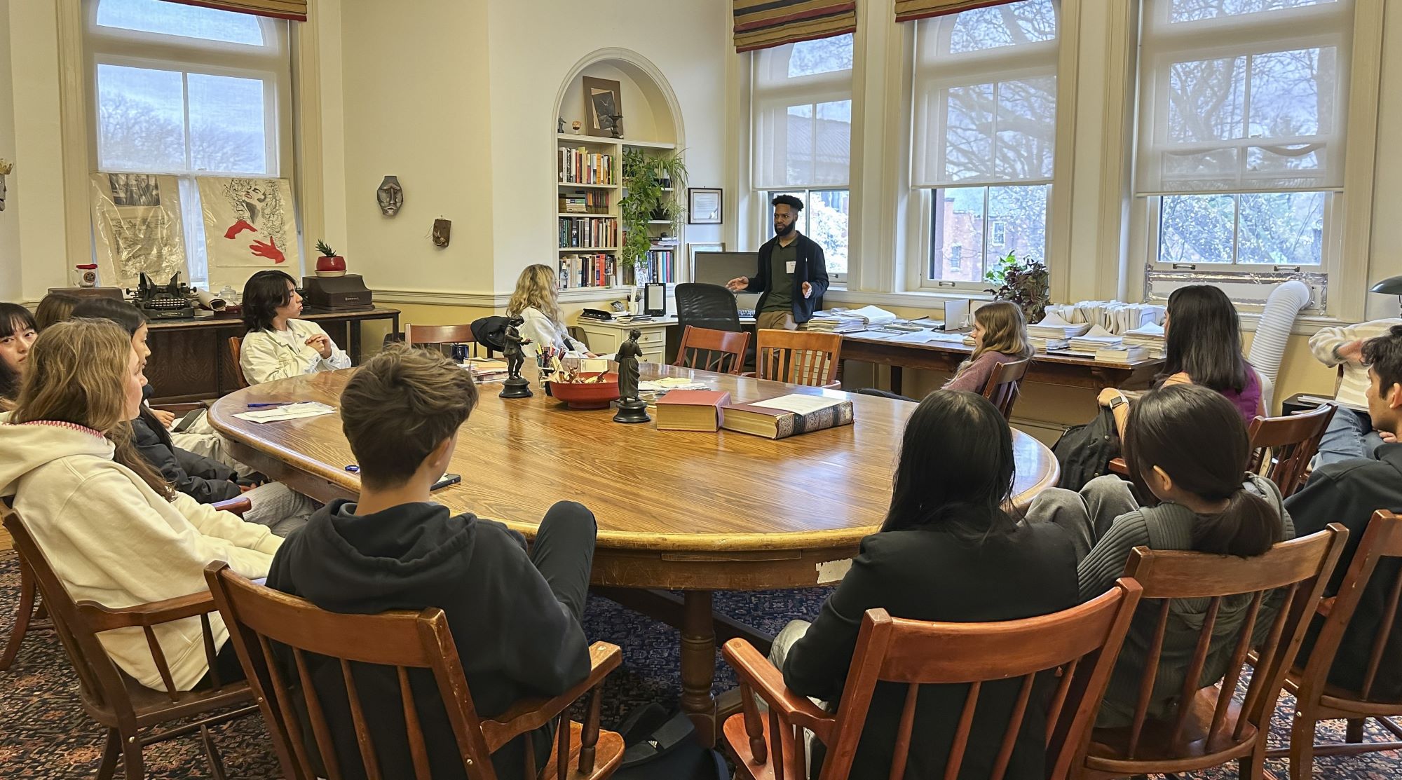 Students at a Harkness table listen attentively to an alumnus discuss his career.