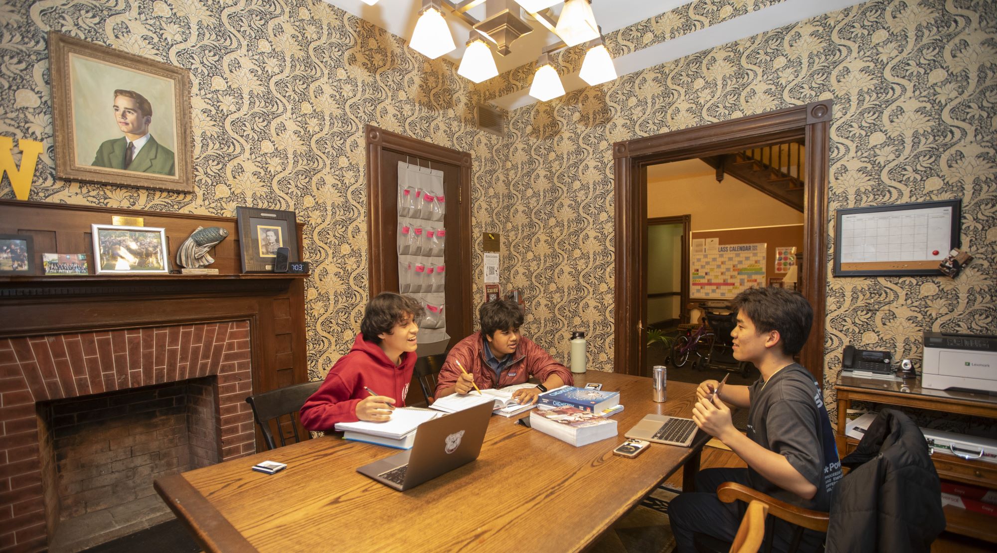 Three boys enjoy a laugh while doing homework in front of the Woodhull House fireplace.