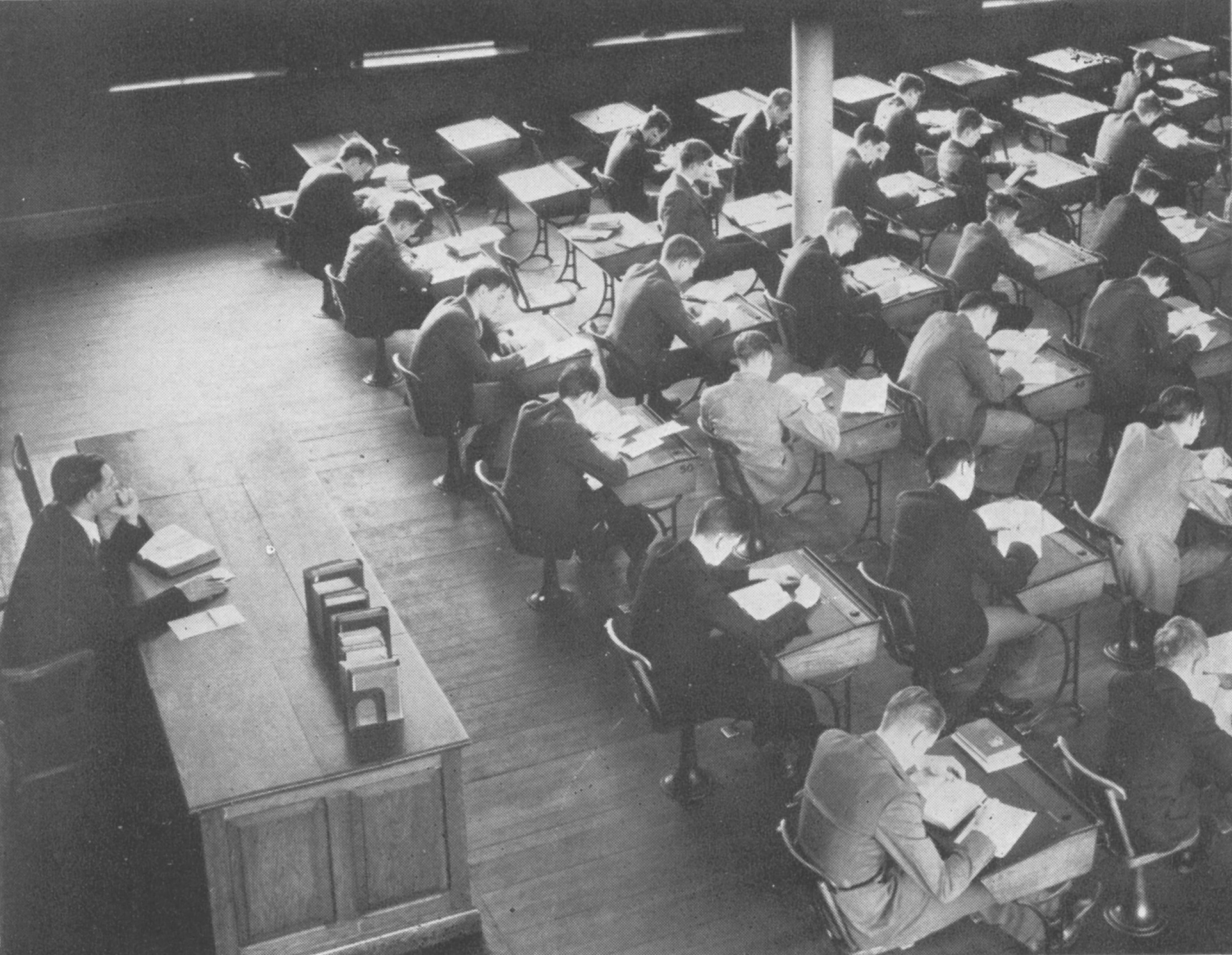 Black-and-white image of students sitting in rows of desks with the instructor sitting behind them. This was the arrangement of classrooms prior to Lawrenceville's adoption of the Harkness method.