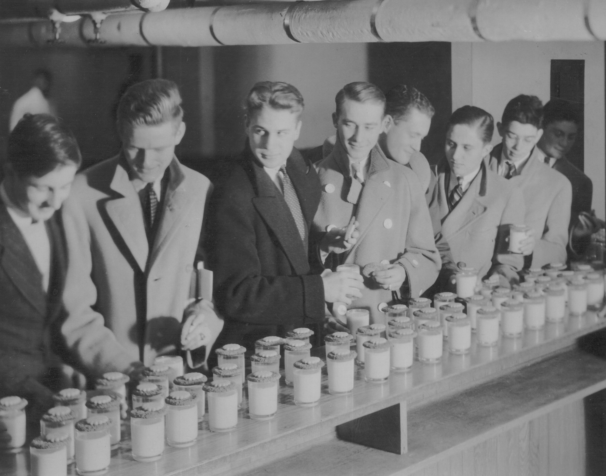 Black and white image from the 1920s or '30s of boys lining up to get their glasses of milk at the old Pop Hall milk bar.