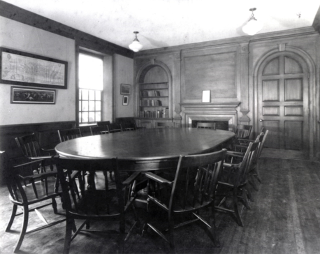 Black and white image of a post-1936 renovated classroom inside Pop Hall, with an empty Harkness table and chairs dominating the room.