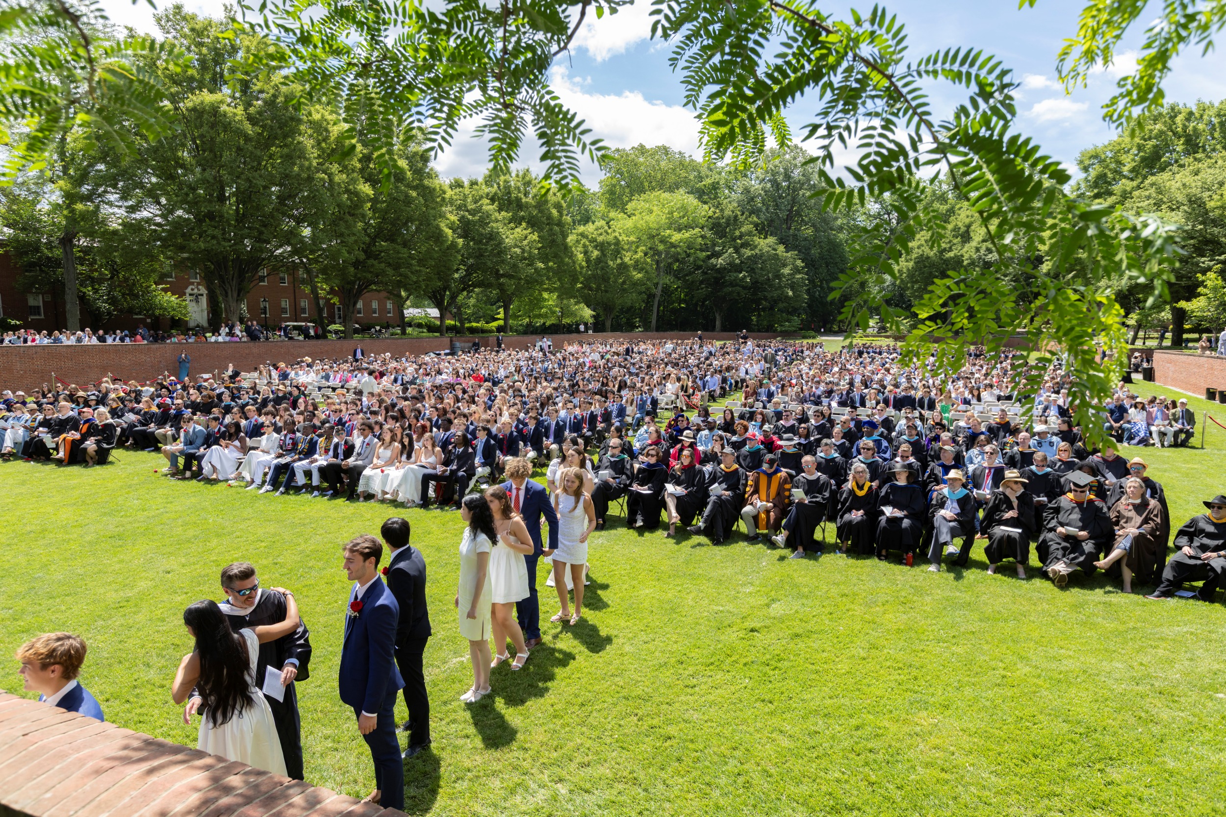 A look from behind and off to the side of the Commencement stage at the assembled crowd on the Bowl, with graduates lining up to collect their diplomas on a sunny day.