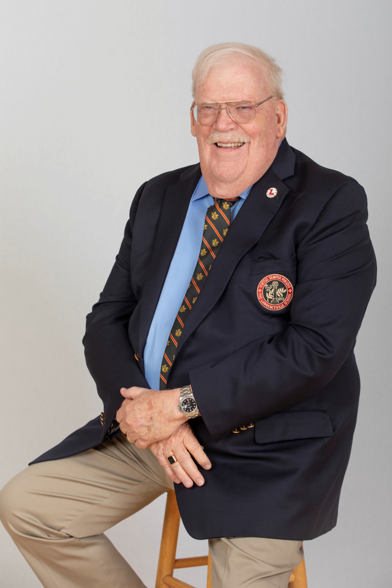 Portrait of Matt Dominy '65 wearing a blue blazer with a Lawrenceville seal and a black, red, and gold Lawrenceville tie over a light blue shirt.