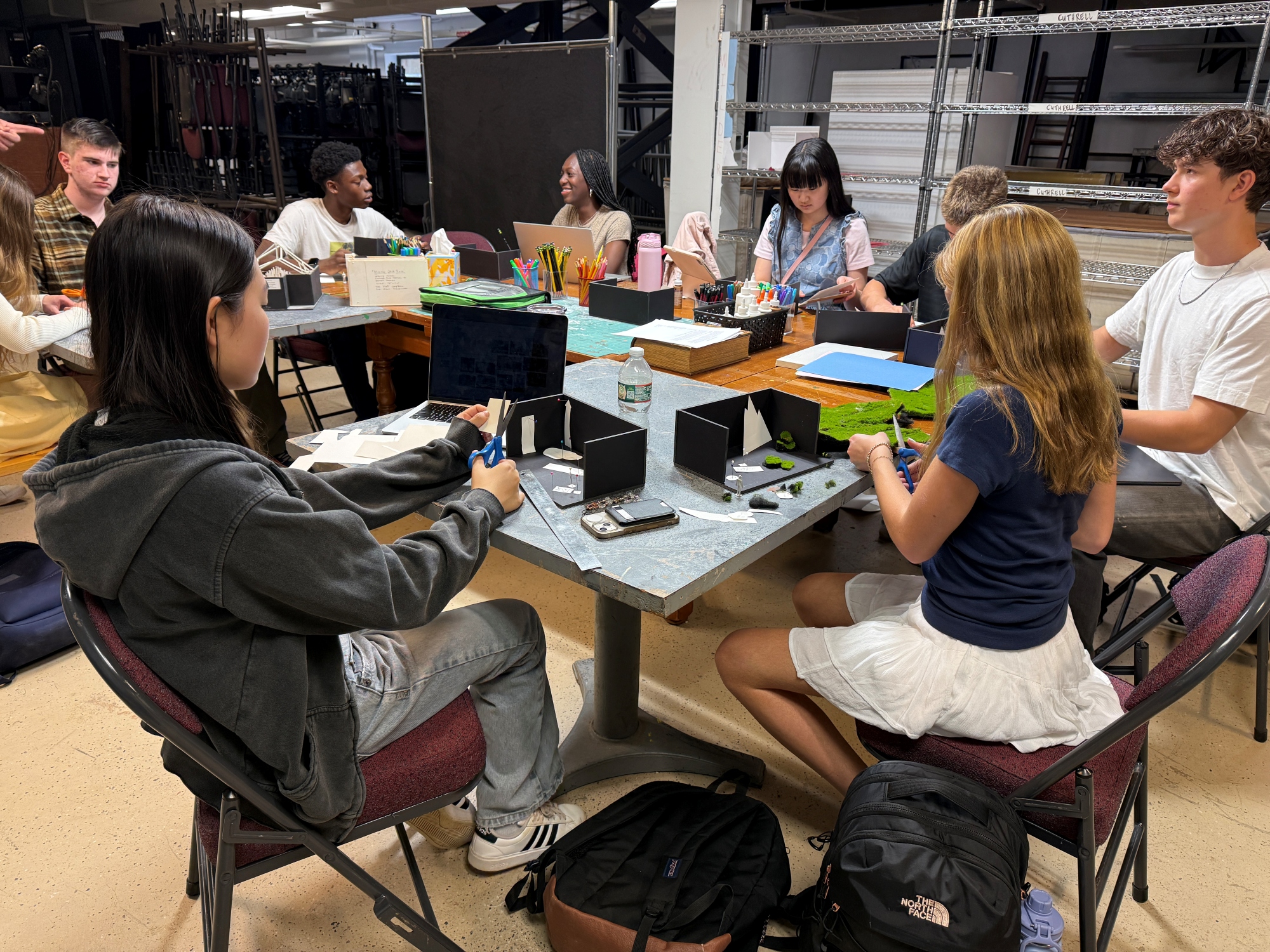 Foundations of Theatre students sit at a table assembling scale models of stage sets.