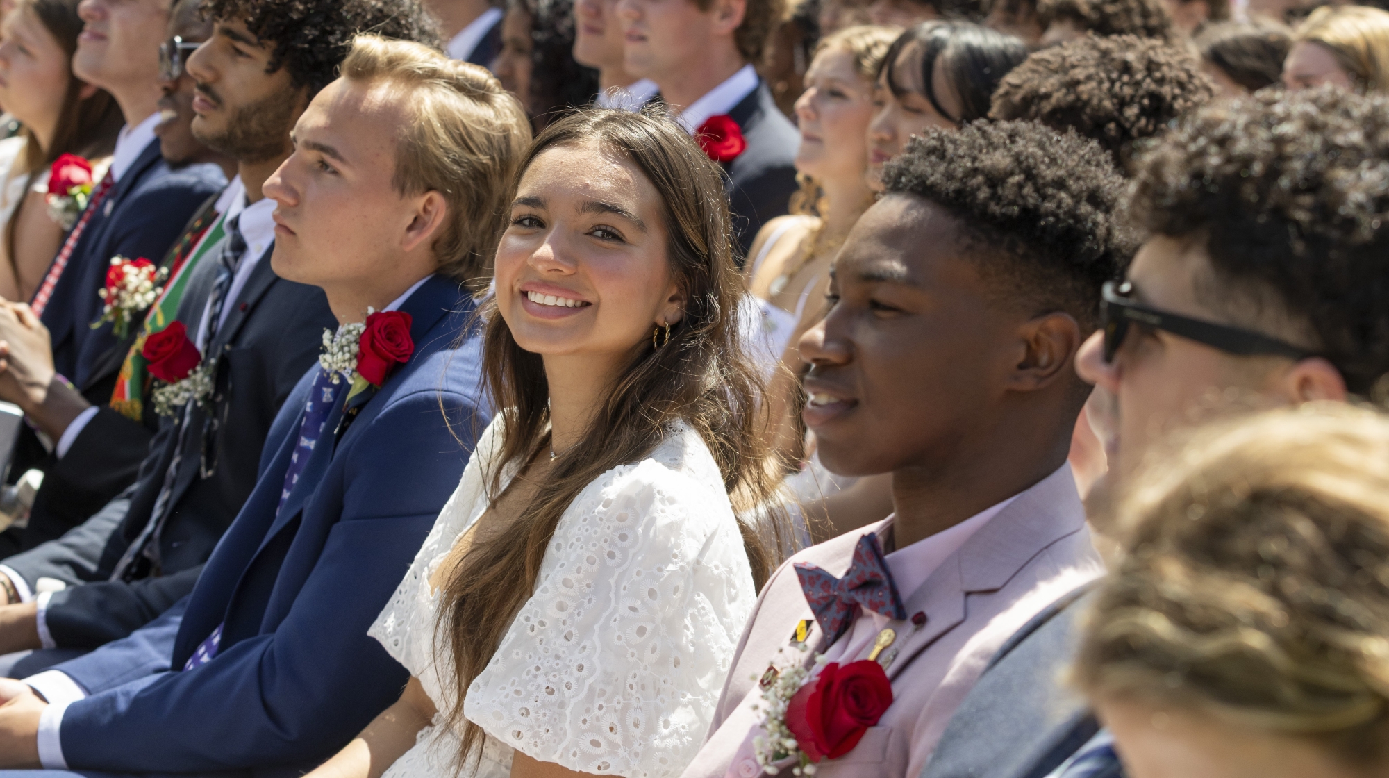 As students sit in rows looking forward in the Bowl at Commencement 2025, one smiling girl noticed a photographer to her left at the end of the row.