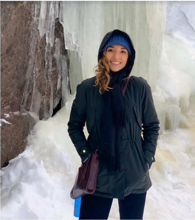 Hannah-Marie Garcia-Ladd '15 standing in a heavy winter coat with her hood up, smiling, in front of a a cascade of ice.