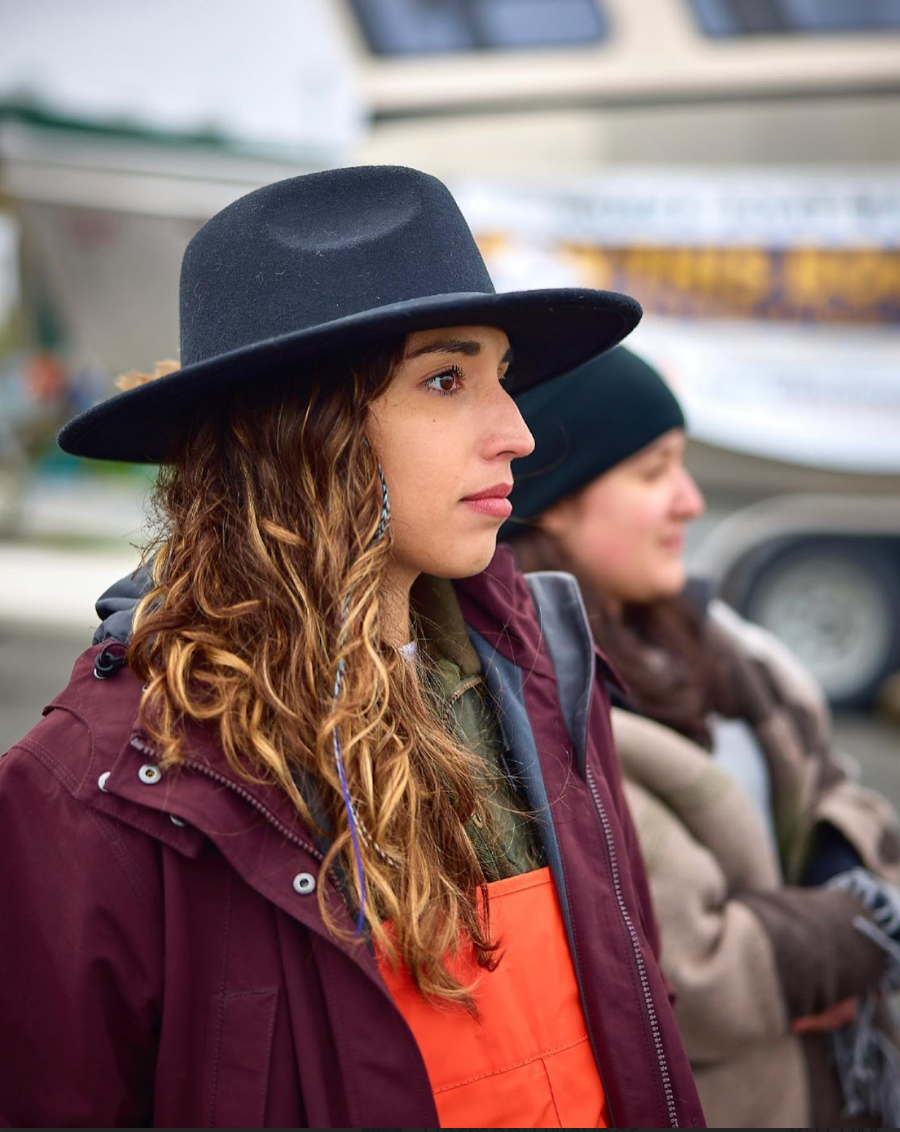Hannah-Marie Garcia-Ladd '15 stares into the distance. She and others are wearing cold-weather boating gear, and Hannah-Marie is wearing a black brimmed hat.