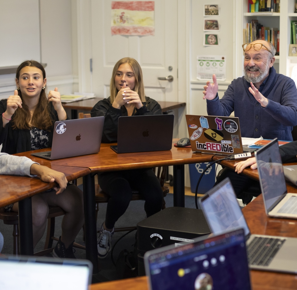 Spanish teacher Joaquin Gonzalez reacts excitedly to a student out of view, as two students to Joaquin's right also react with enthusiasm.