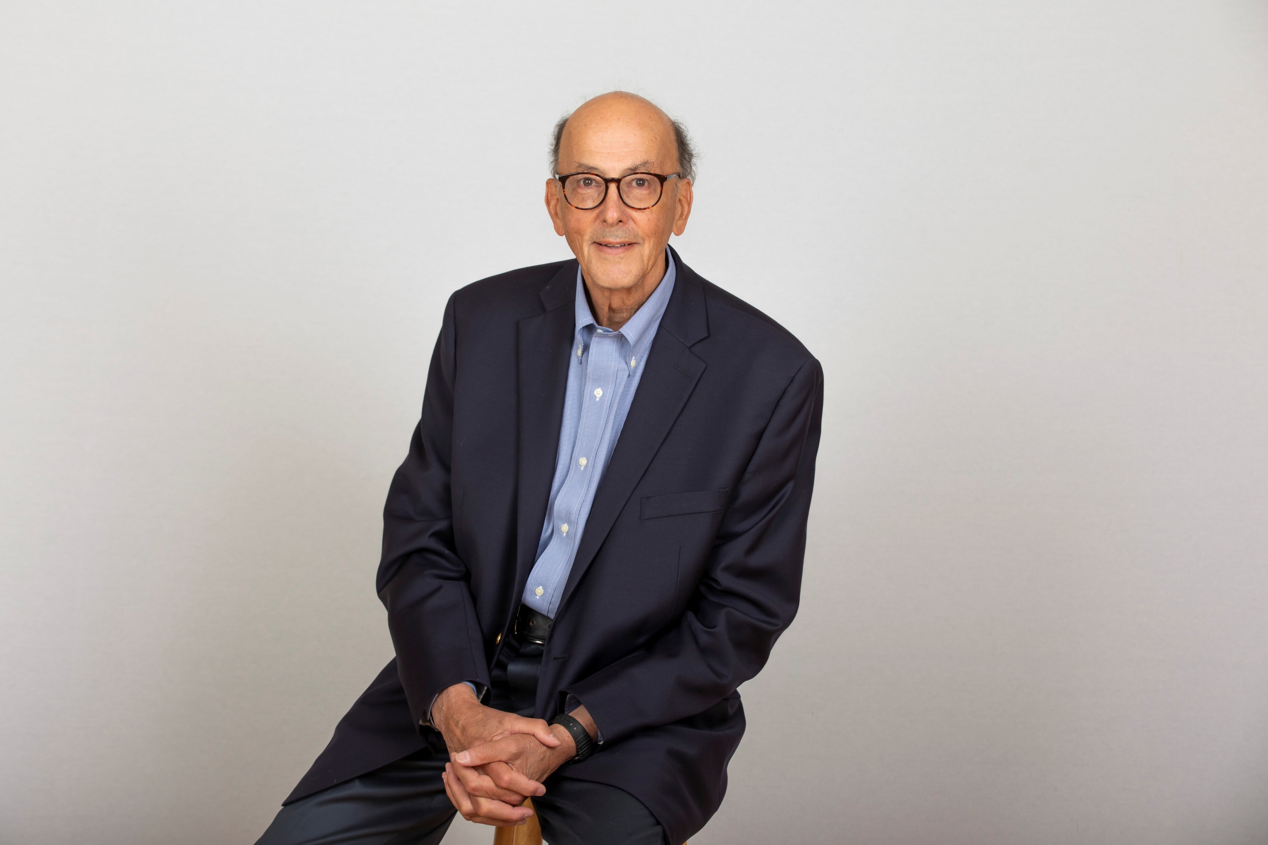 Portrait of Roger Glass '63 wearing a navy blazer over a light-blue shirt with his arms folded.