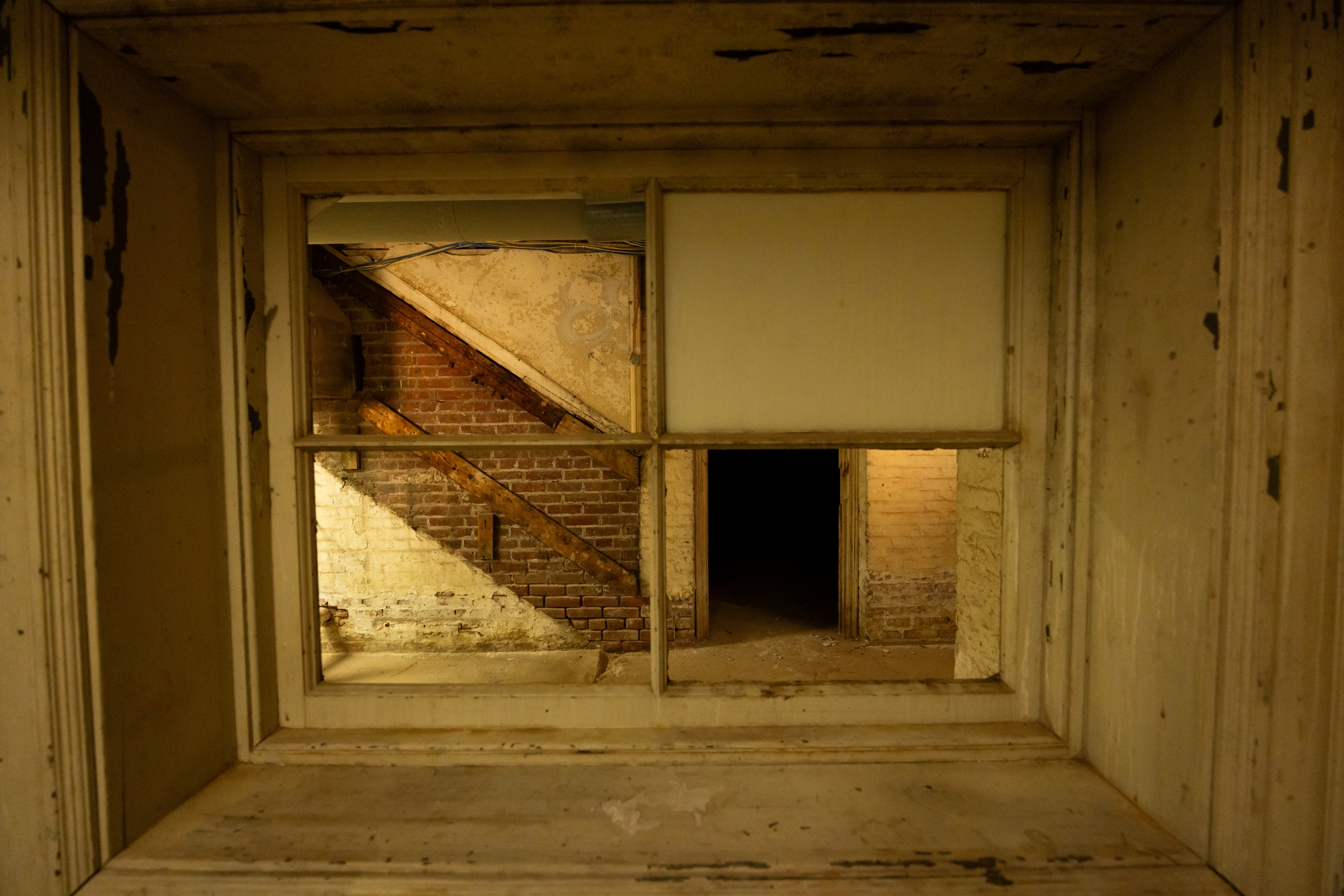 Looking through what was once an exterior window in the basement of Upper House, you see the unpainted outline of where a staircase used to climb the brick wall toward the the ground level floor of Upper.