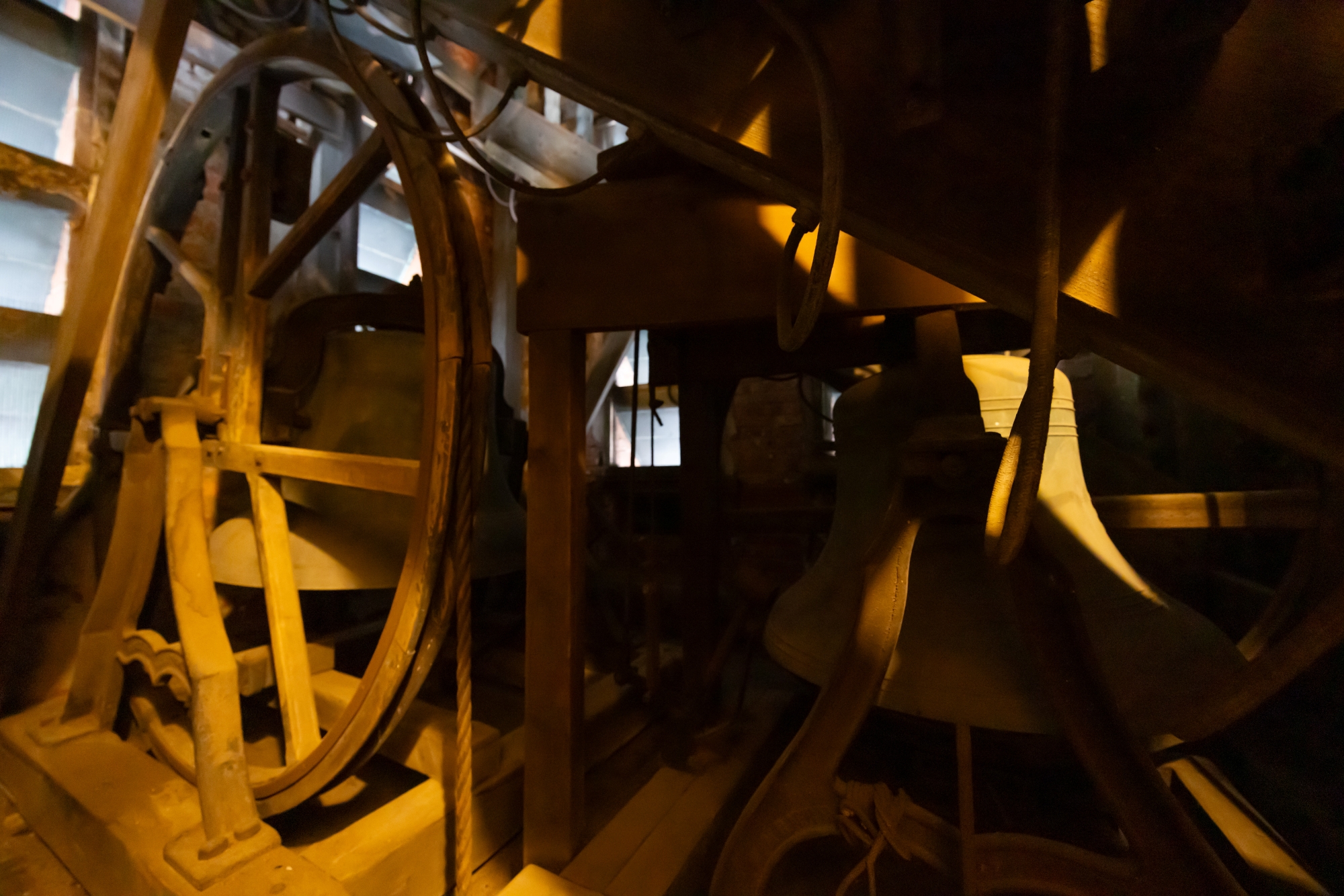 In dappled sunlight, you can see shadows and light alternate on the bells and the old wood-and-metal pulley wheel.