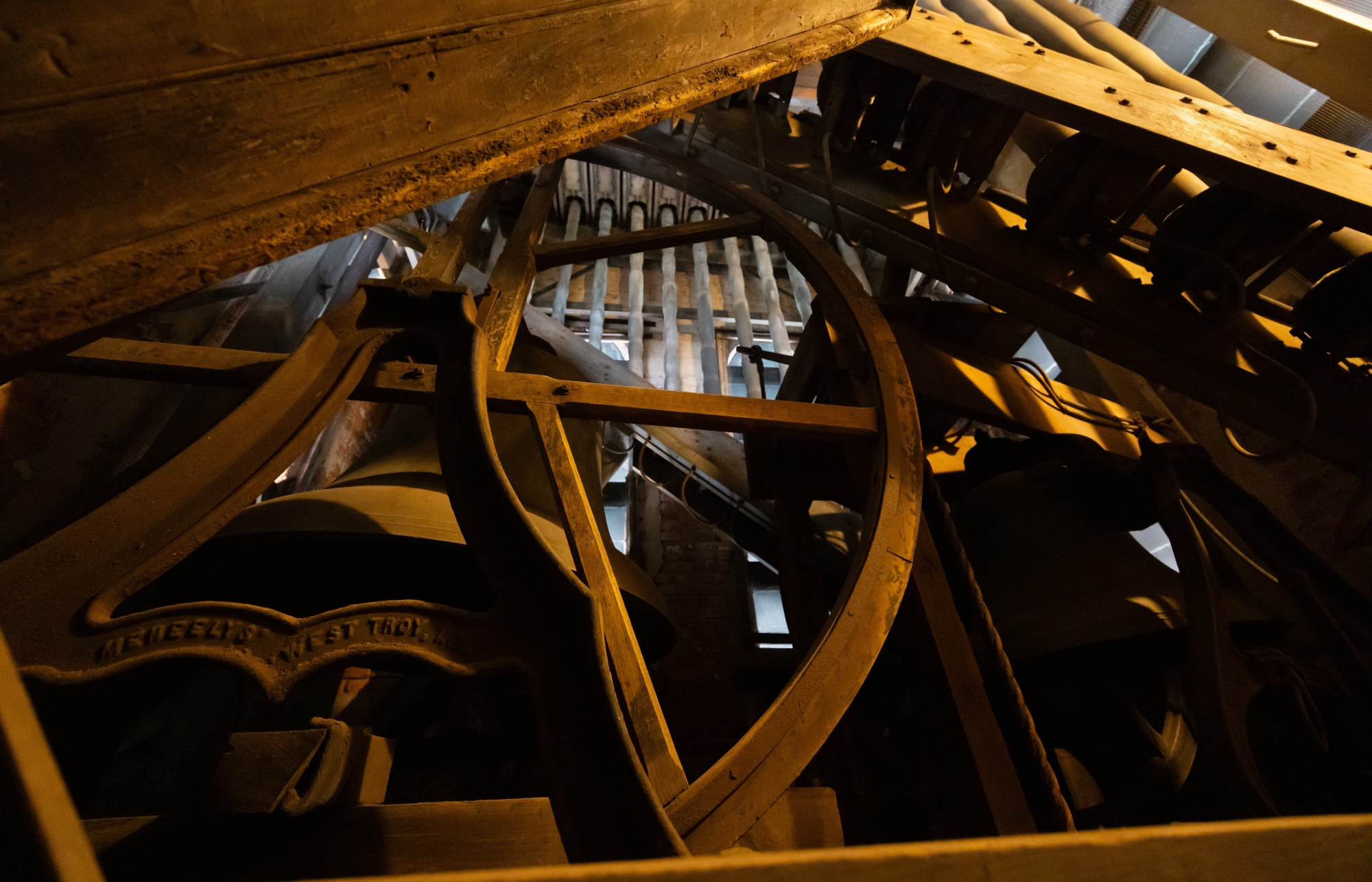 In dappled sunlight, you can see shadows and light alternate on the bells and the old wood-and-metal pulley wheel.