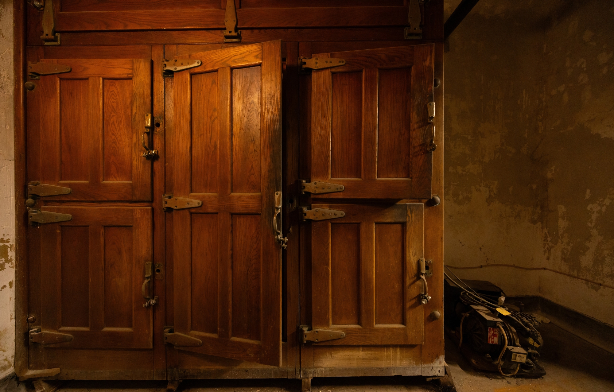 A century-old golden wood-clad refrigerator sits in a dim room with the center of its three doors slightly ajar.