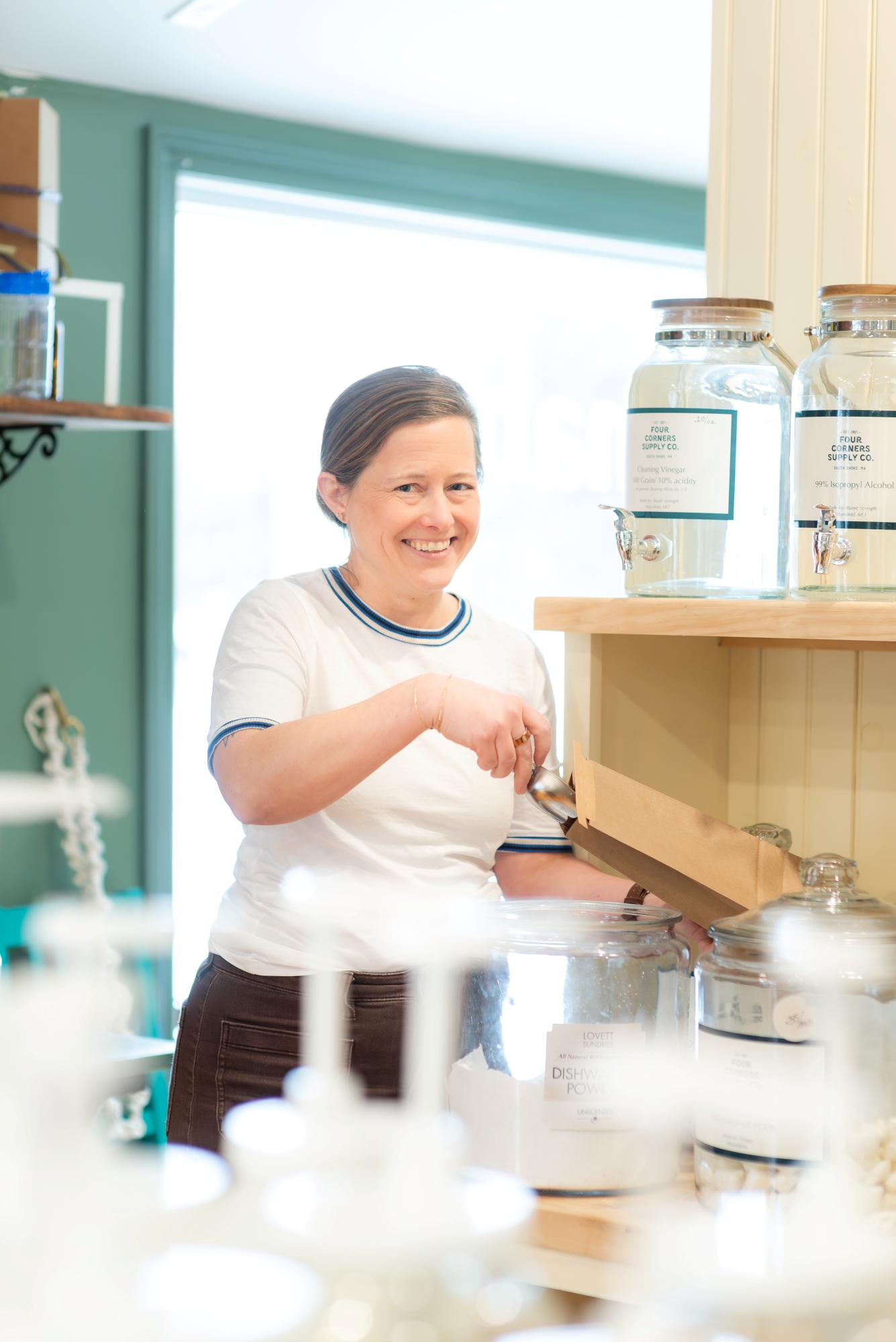 Julia Traggorth '05 is wearing a white ringer T-shirt with dark blue banding and brown corduroy pants. She is smiling as she scoops a product into a small beige paper bag.
