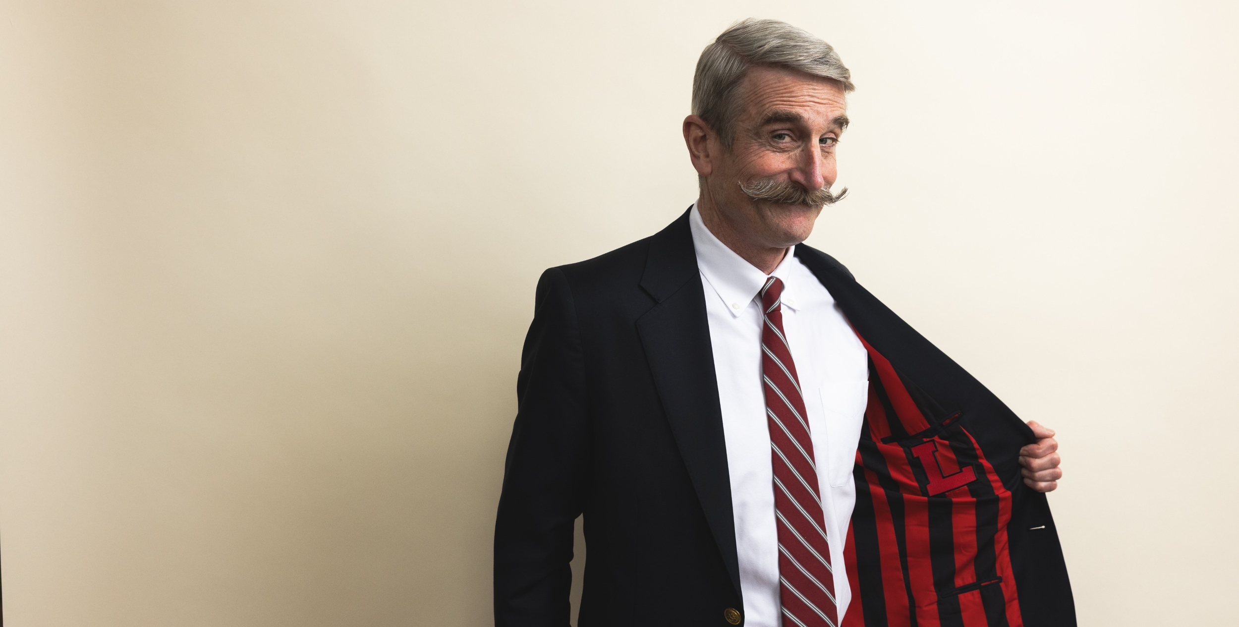 A playful, impish smile is on the face of Steve Murray as he pulls open the left side of his blue blazer to reveal red and black vertical stripes and a block Lawrenceville "L" emblazoned on the pattern.