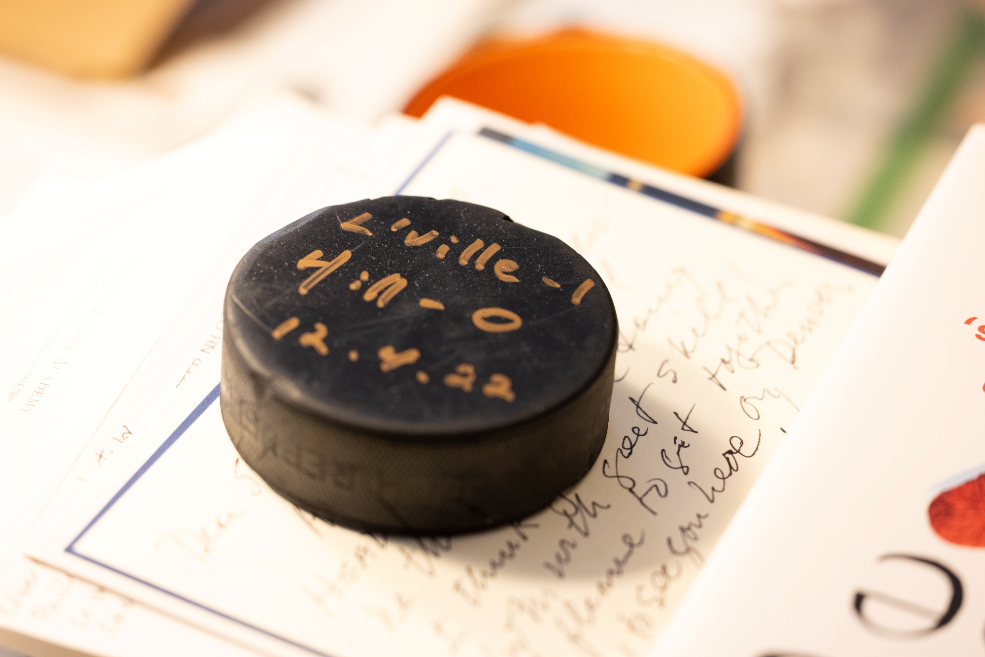 A hockey puck from a 2022 Lawrenceville-Hill ice hockey game with the score, Lawrenceville 1, Hill 0, written in gold ink.