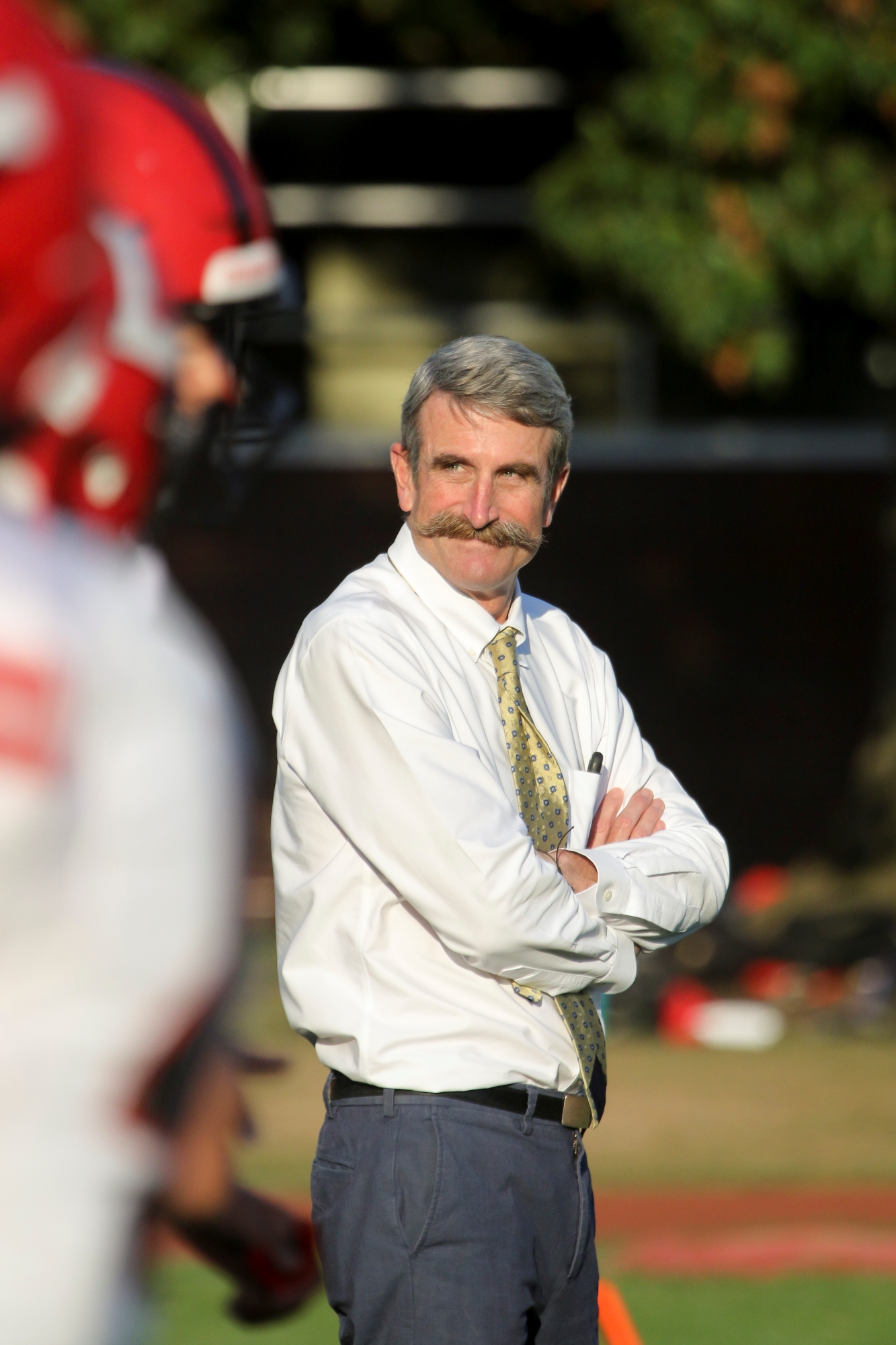 Steve Murray, wearing a white shirt and a light colored tie, has his arms folded as he looks off to action on his right side.