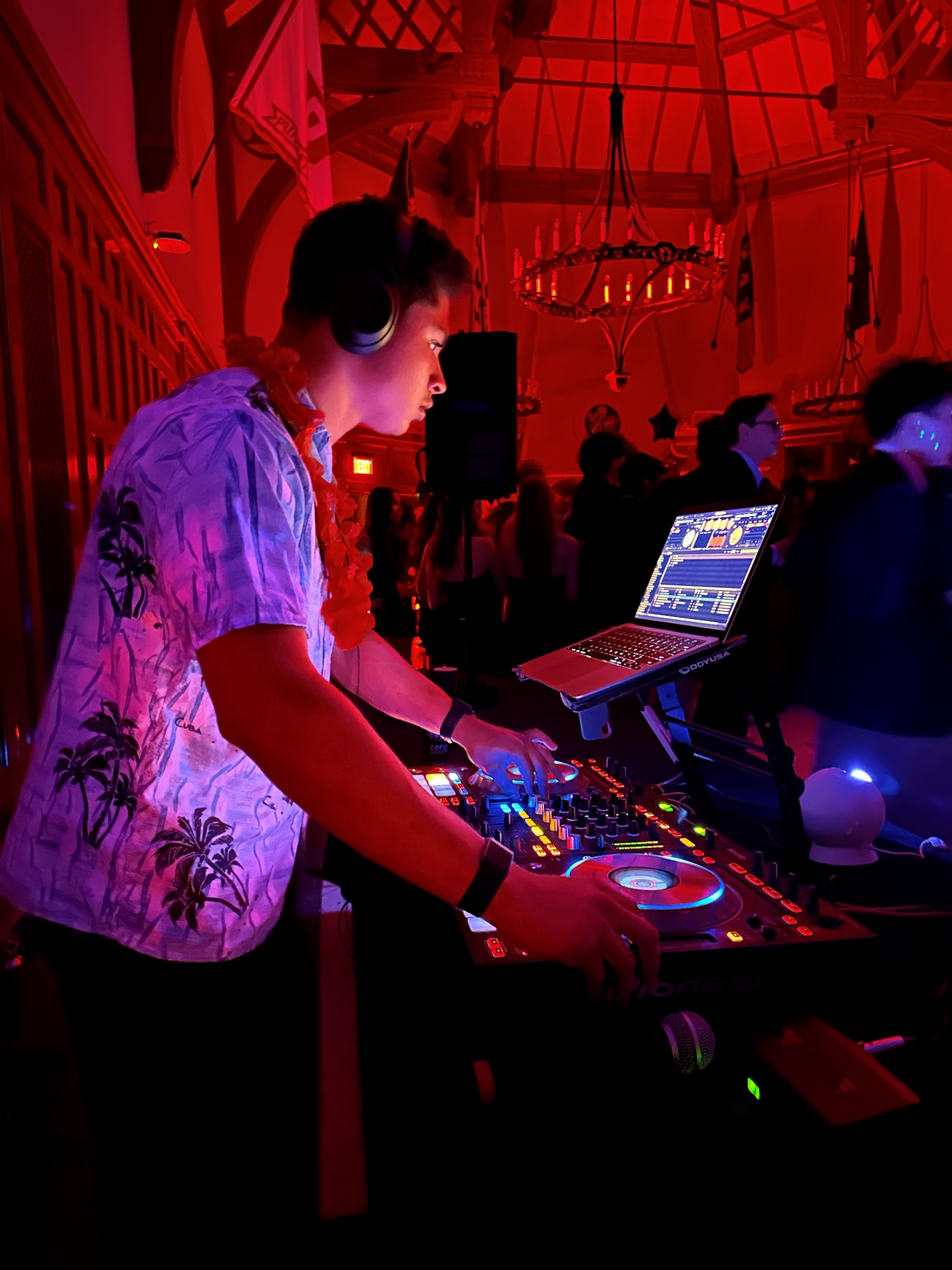 In a room lit red and darkened for a student dance, Alex Salgado-Lozhkin '26 deejays at his equipment board while wearing headphones